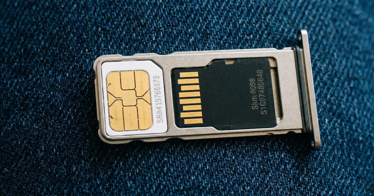 Open phone SIM tray showing a nano-SIM card and a microSD card side by side in the same slot, dark blue background