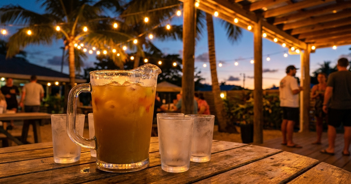 Pitcher of kava mixed with tropical juice and ice on an outdoor table at dusk, string lights, warm tones