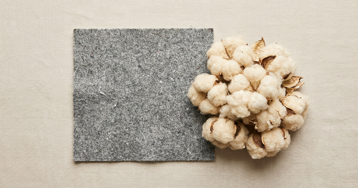 A swatch of recycled polyester fabric laid next to raw organic cotton bolls on a neutral background, representing the recycled polyester vs organic cotton comparison A swatch of recycled polyester fabric laid next to raw organic cotton bolls on a neutral background, representing the recycled polyester vs organic cotton comparison