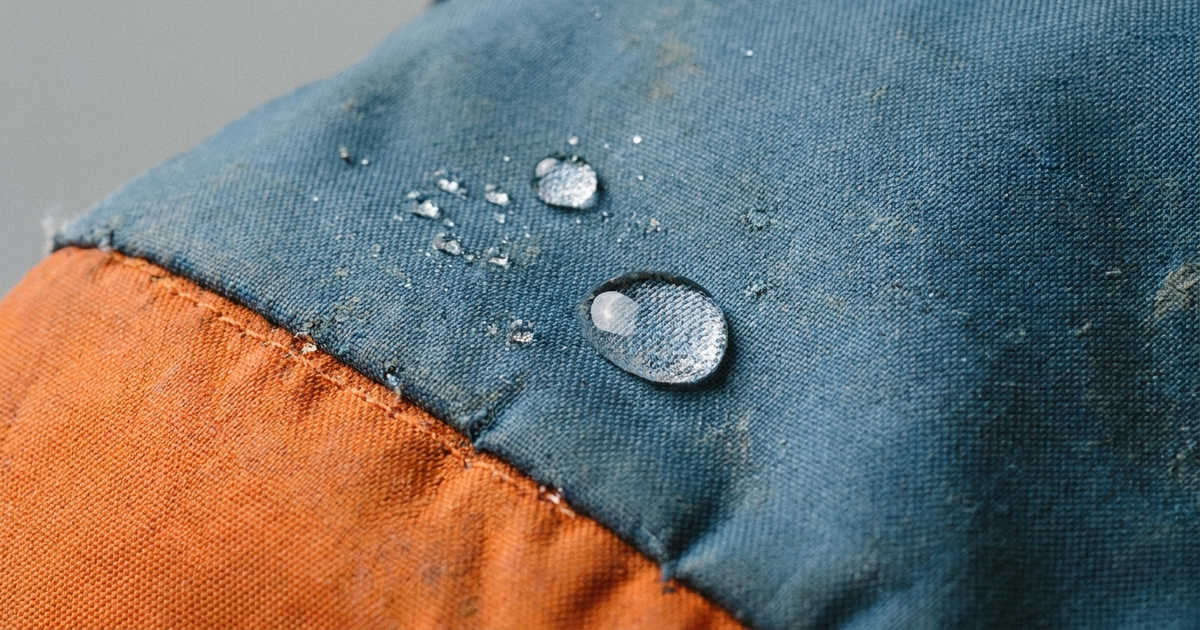 A child's school backpack with a water droplet beading off the fabric surface, close-up texture shot, neutral studio bac A child's school backpack with a water droplet beading off the fabric surface, close-up texture shot, neutral studio bac